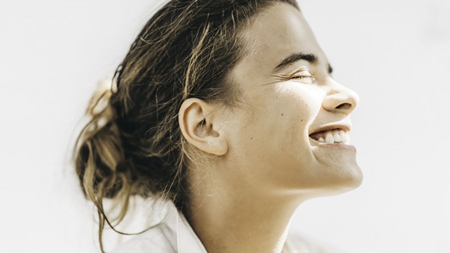 Mulher de olhos fechados e a sorrir, representando o impacto da menopausa na sa&uacute;de oral