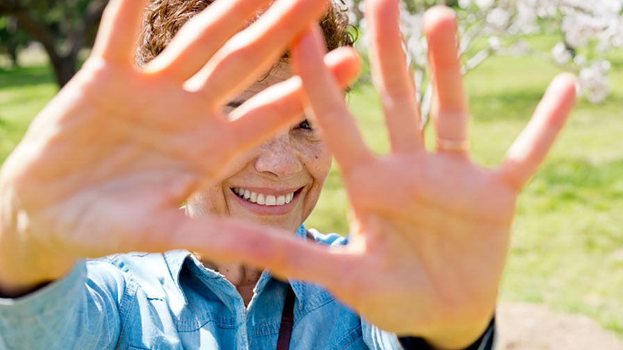 Mulher ao ar livre, a sorrir e a mostrar as m&atilde;os, simbolizando cuidados com a sa&uacute;de oral na menopausa